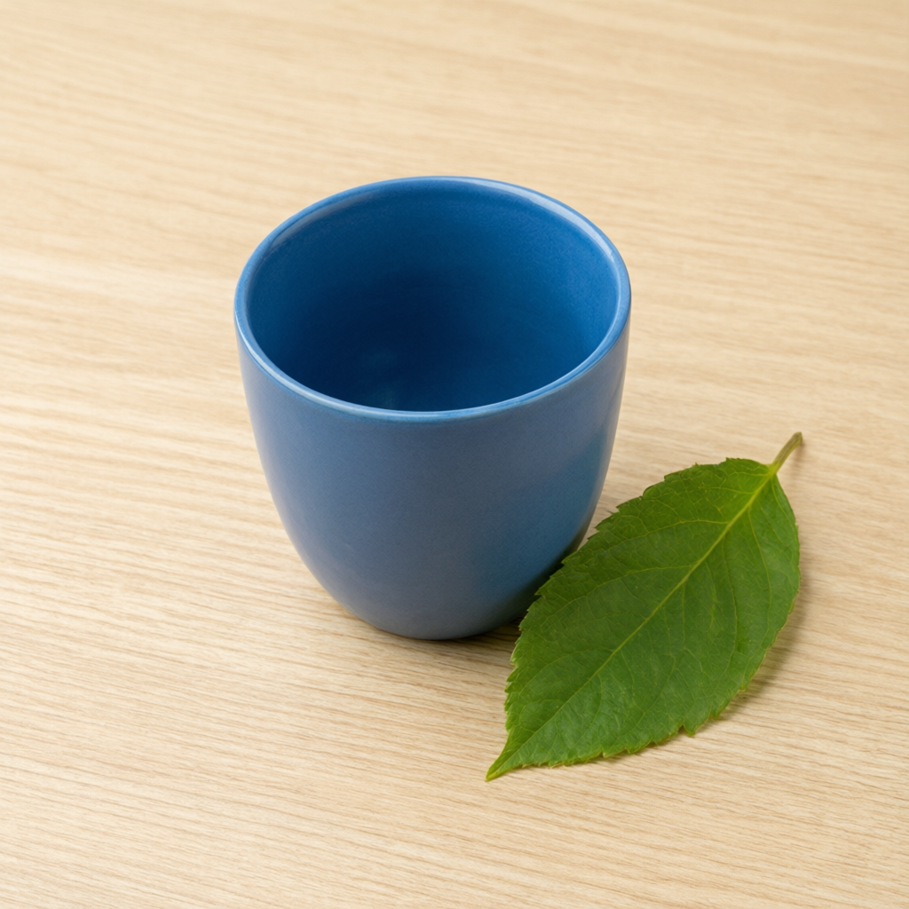 Qwen Image 3 sample: A single blue ceramic cup and green leaf on a light wooden desk, clean natural daylight, no text.