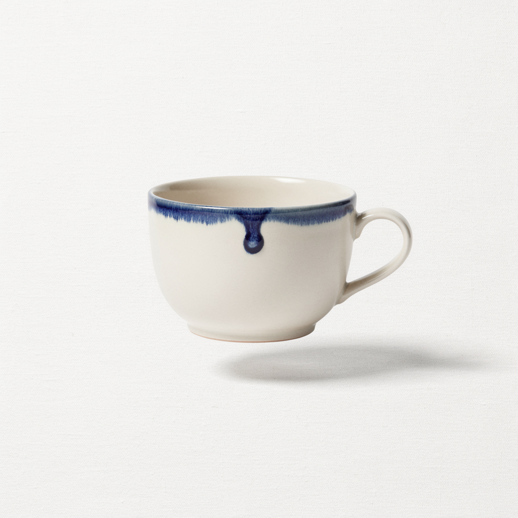Minimalist e-commerce packshot: a single handmade ceramic espresso cup with a cream matte glaze and a tiny cobalt drip, floating on a pure #F5F2EC linen backdrop. Shadow hand-softened beneath. 1:1 framing, overhead-soft key at 30°, 85mm f/5.6. Cup fills 60% of frame, breathing room. Shopify-grade, catalog-ready, sharp edge-to-edge.
