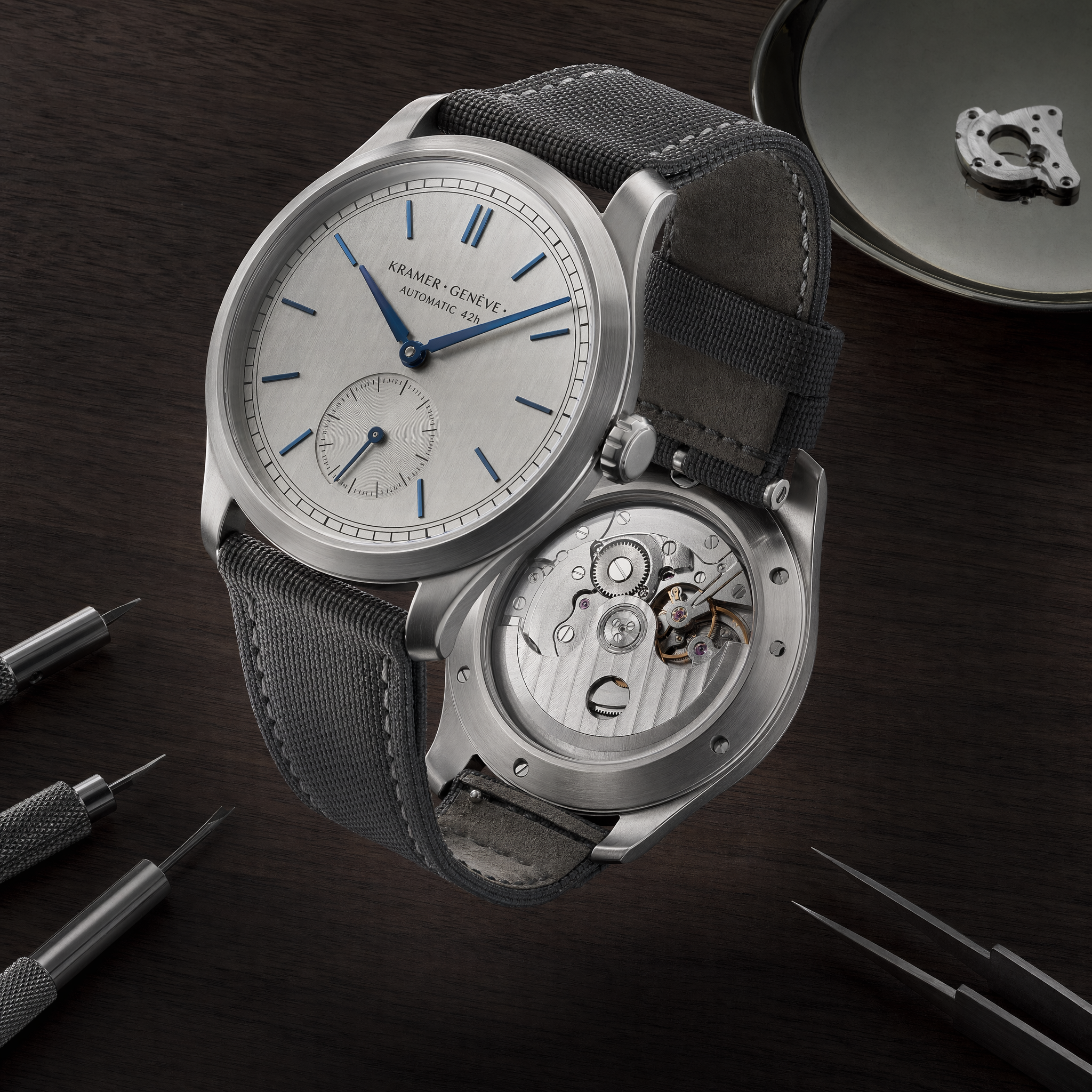 4K hero shot for a fictional Swiss brand. A brushed titanium mechanical wristwatch, open caseback showing movement, suspended above a black walnut desk at 45° angle. Dial text reads exactly "KRAMER · GENÈVE · AUTOMATIC 42h". Blue polished hands, no logo on crown. Studio softbox 60°, rim light at 210°, f/11 focus-stack sharp edge-to-edge. Catalog-grade, no backdrop blur, no compositing seams.