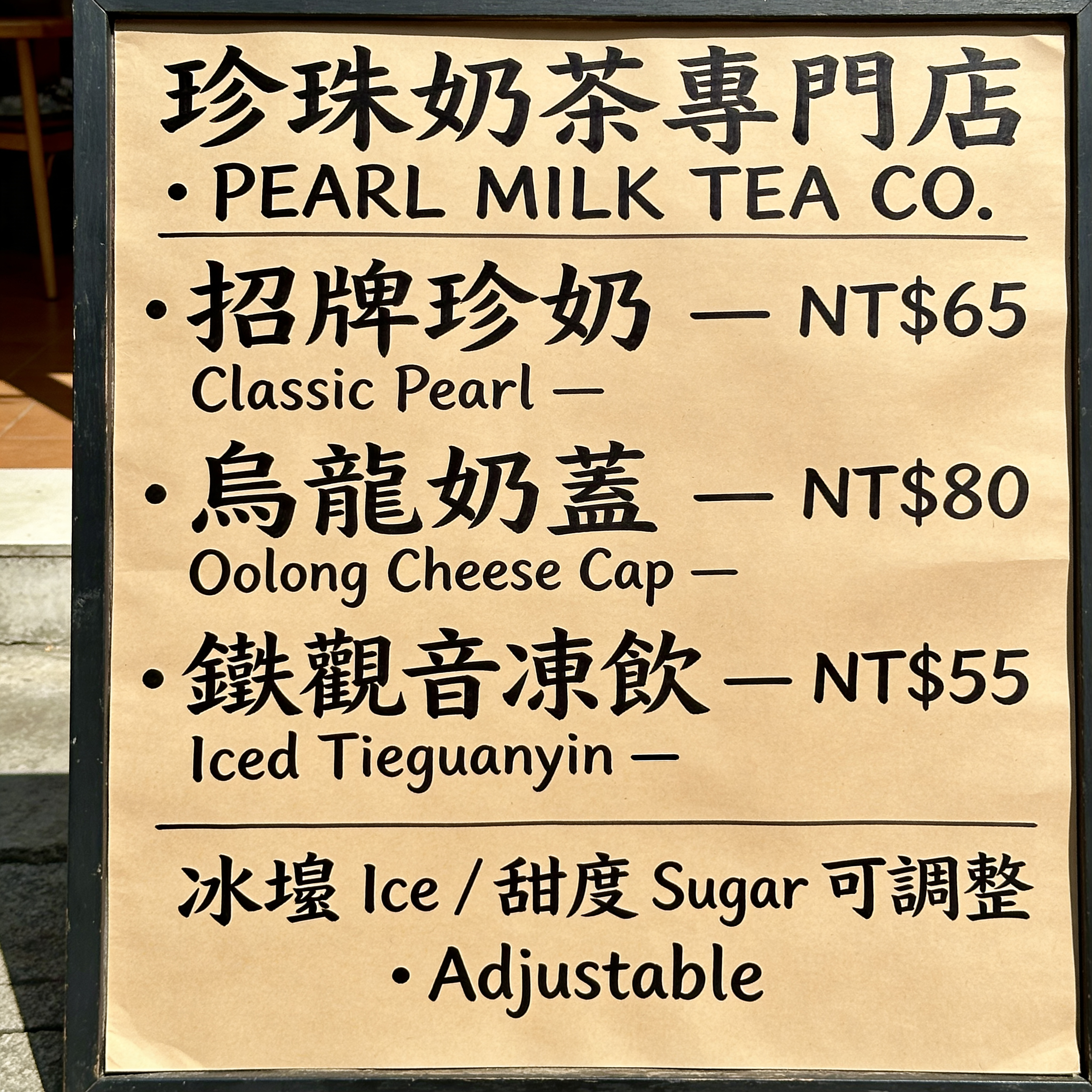Taiwanese bubble tea shop menu board, vertical, photographed straight-on in afternoon light. Traditional Chinese + English bilingual layout. Title reads exactly "珍珠奶茶專門店 · PEARL MILK TEA CO.". Below, three rows of items with exact prices:
• 招牌珍奶 Classic Pearl — NT$65
• 烏龍奶蓋 Oolong Cheese Cap — NT$80
• 鐵觀音凍飲 Iced Tieguanyin — NT$55
Footer line reads exactly "冰塊 Ice / 甜度 Sugar 可調整 · Adjustable". Handwritten-marker aesthetic on kraft, legible at full crop, no duplicated items.