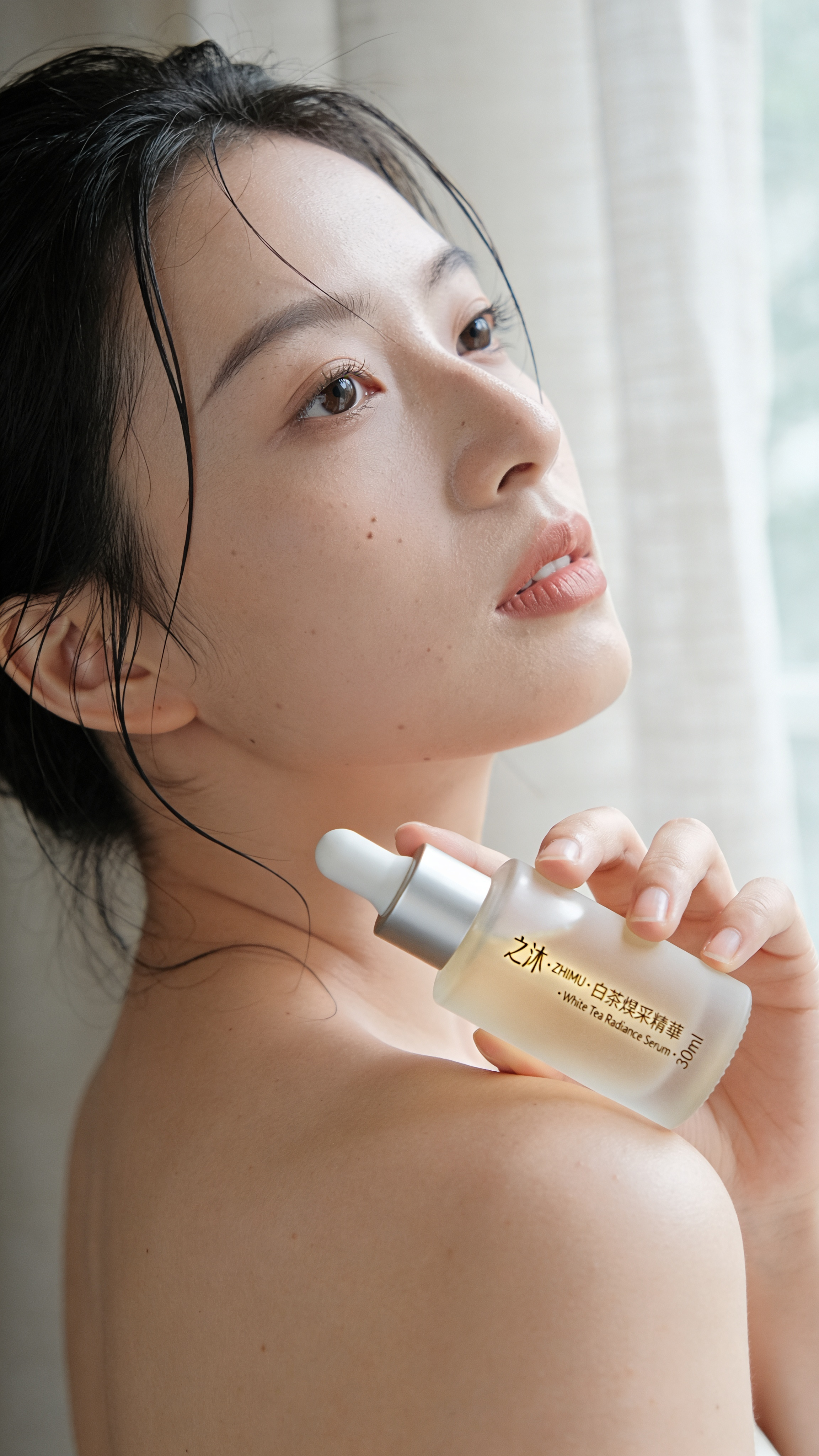 Editorial lifestyle shot for a fictional Shanghainese skincare brand. A young Asian woman, 28, with bare shoulders and damp hair, holds a frosted glass serum bottle near her collarbone. Bottle label reads exactly "之沐 · ZHIMU · 白茶煥采精華 · White Tea Radiance Serum · 30ml" in vertical gold leaf. Soft north-window light, linen curtain out of focus. Portra 400 palette, skin pores visible, no beauty retouch. Chinese and English both rendered correctly.